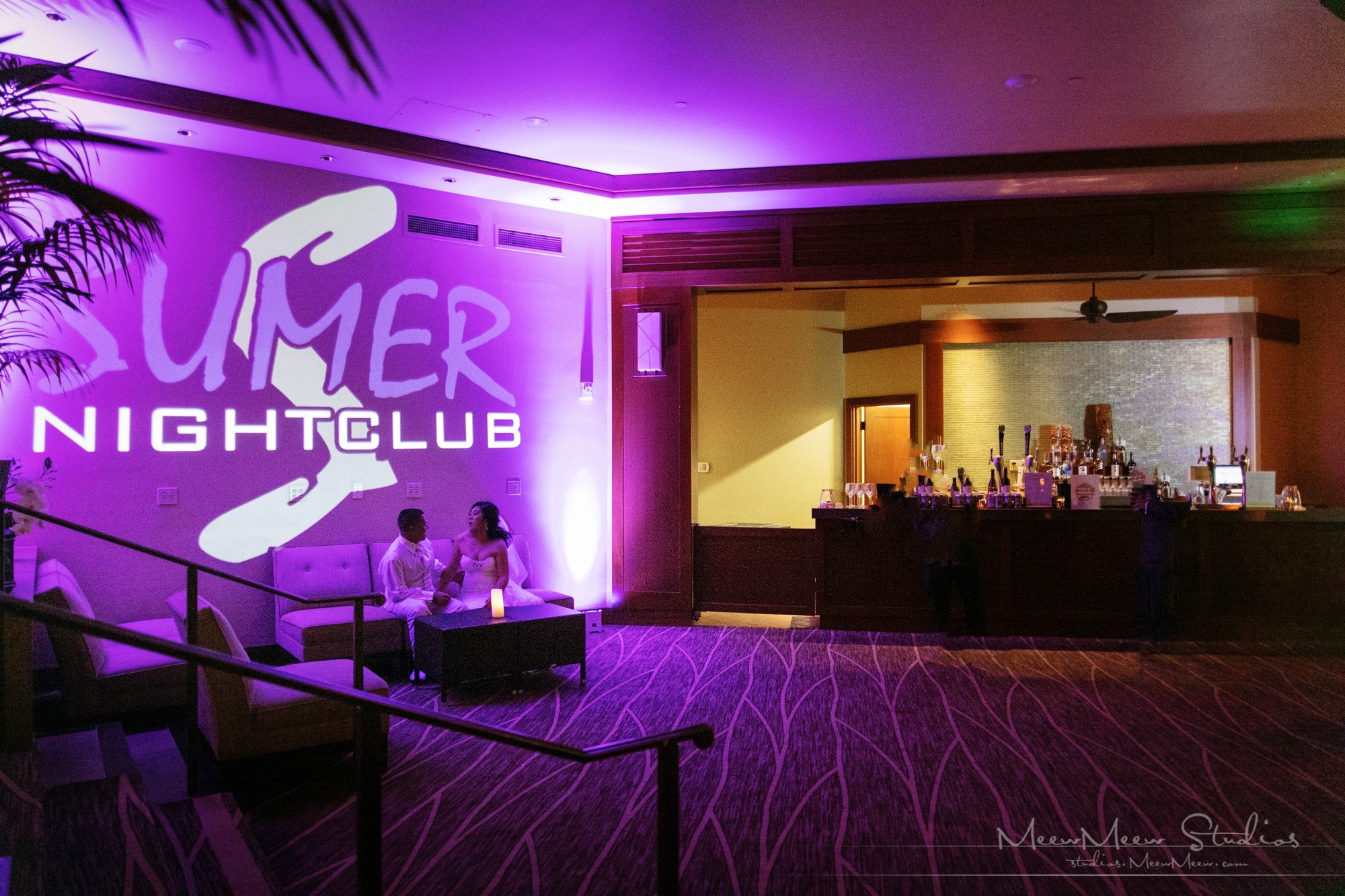 A couple chats in a club lounge area with purple lighting and a bar in the background.