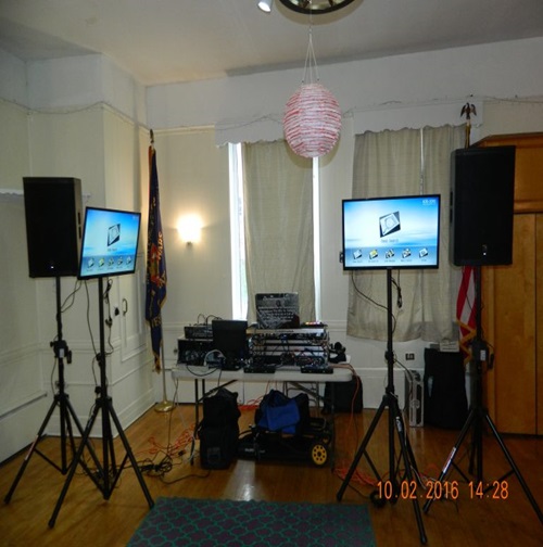 DJ karaoke setup with two large screens, speakers, and control boards.