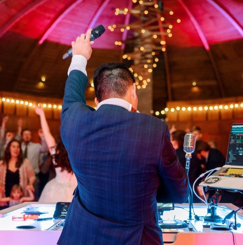 DJ hyping up the crowd from behind the booth at a wedding party.